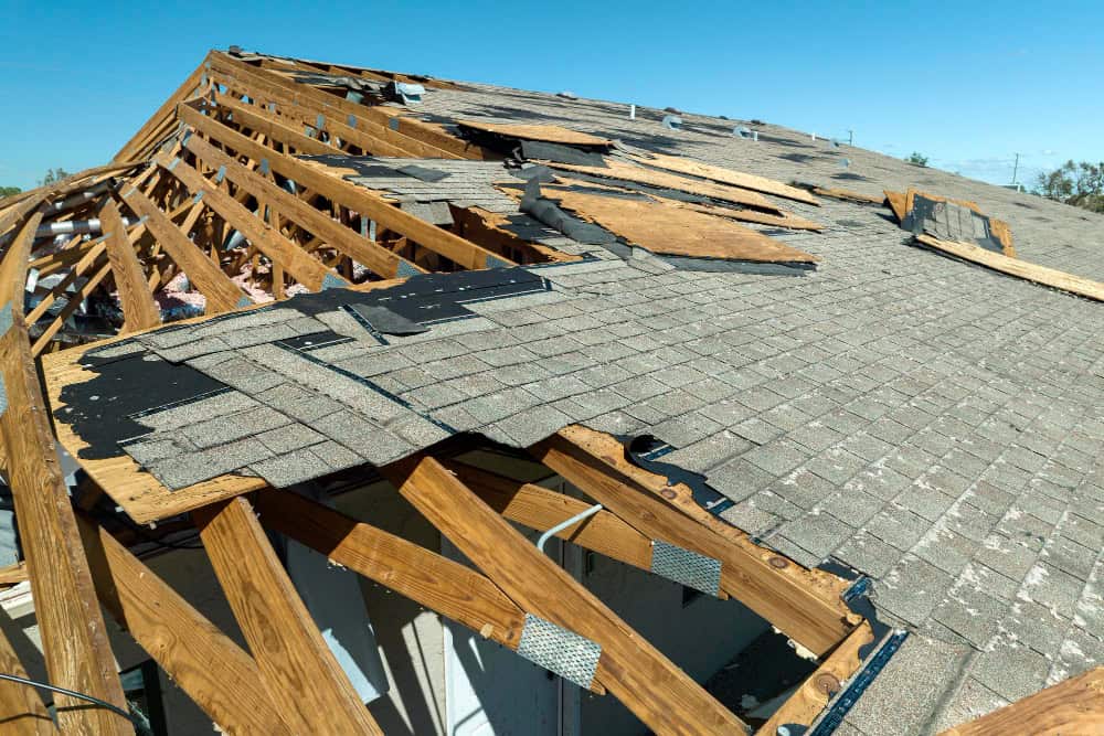 Storm-damaged roof with exposed trusses before repair